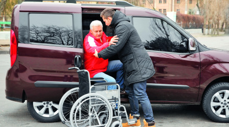 Young man helping handicapped man to sit in wheelchair