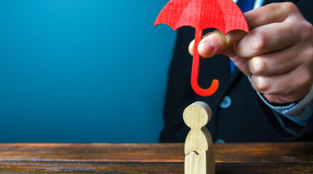 Un homme protège une figurine de bois avec un parapluie rouge.