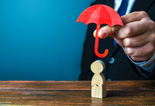 Un homme protège une figurine de bois avec un parapluie rouge.