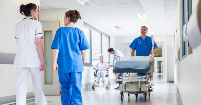 Male nurse pushing stretcher gurney bed in hospital corridor wit